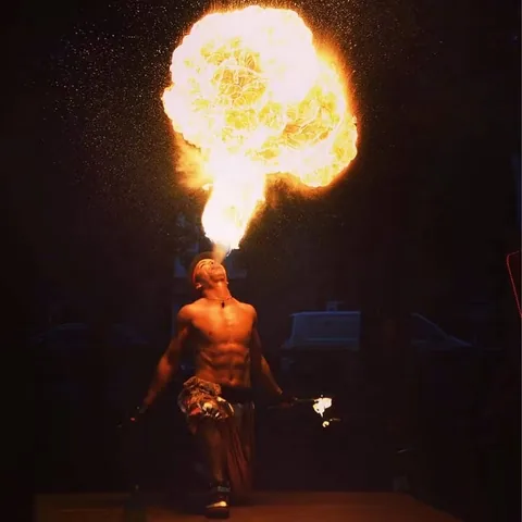 Fire breather Nuno with two torches blowing a large fireball straight up into the night