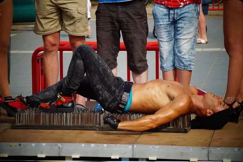 Fakir act in the street: two spectators standing on Nuno while he lies on the bed of nails