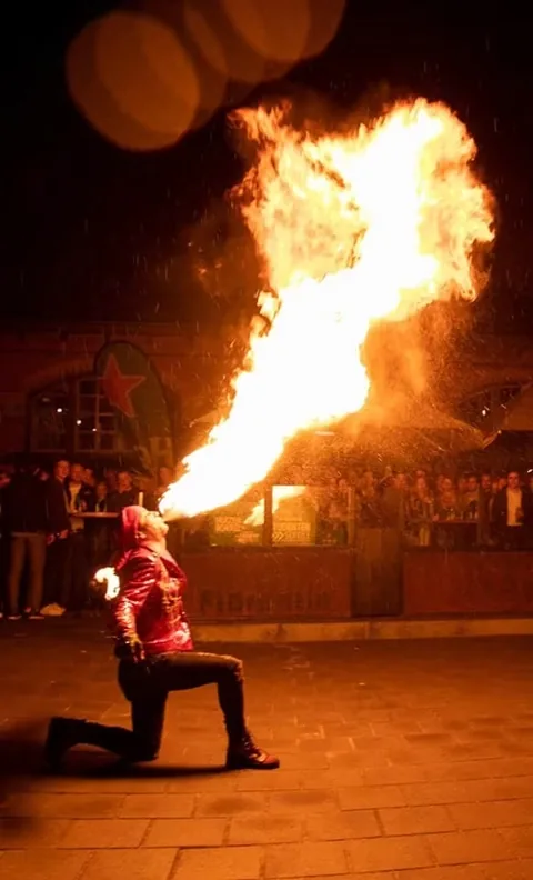 Kneeling, fire breather Nuno blows a long flame across the terrace, even in the rain