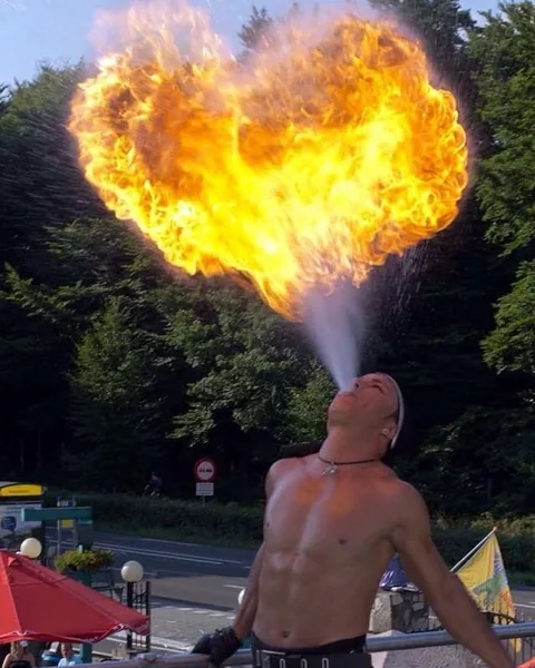 Fire breather Nuno blowing a heart-shaped fireball against the summer sky