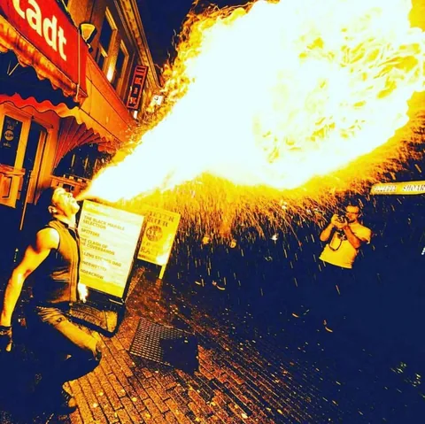Fire breather Nuno blowing an enormous sea of fire with a rain of sparks in a nightlife street